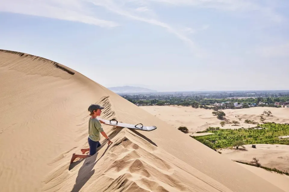 Boy preparing to practice sandboarding in the Huacachina dunes | Ultimate Trekking